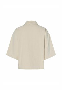 Kratki rukavi, bež srajca s ovratnikom. Škatlasta oblika in mehak material, z minimalističnim dizajnom, brez vidnih zapirnih elementov ali vzorcev.