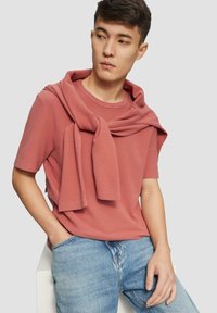 Korte mouwen, geribbelde shirt in stofroze met een zachte trui over de schouders; gecombineerd met lichtblauwe denim jeans.