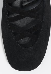 Czarny zamszowy but z okrągłym noskiem, z krzyżującymi się paskami i fakturowanym czarnym wnętrzem. Gładkie szwy i minimalistyczny design.