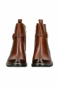 Botas de tobillo de cuero marrón con un acabado suave, que cuentan con una correa texturizada y herrajes en tono dorado. Punta redondeada y suela negra.