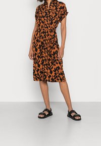 Lyhythihainen, kauluksellinen mekko, jossa oranssi-musta eläinkuosi. Mekossa on joustava vyötärö ja se ulottuu pohkeen puoliväliin. Yhdistetty mustien sandaalien kanssa.