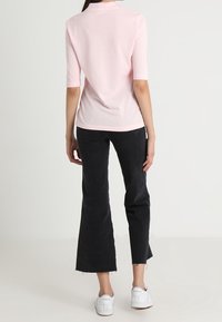 Světle růžový top s krátkým rukávem, přiléhavý střih, měkká textura. Kombinovaný s černými vysokými rozšířenými džíny, oslí okraj a bílými teniskami.