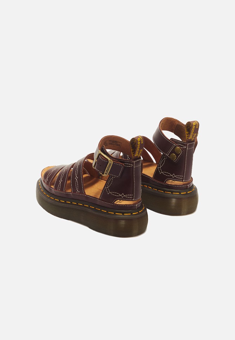 Pair of dark brown leather platform sandals with buckle straps, yellow stitching, and branded heel pull tabs on a white background.