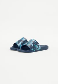 Modre sandale na plaži z cvetličnim vzorcem v teal in beli barvi. Gladek plastičen zgornji del, odprt dizajn za prste, teksturiran podplat in enobarven podplat.