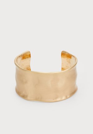 Bracciale in argento con finitura dorata, caratterizzato da una superficie liscia e ondulata, con un interno testurizzato e un design aperto, che crea una forma organica.