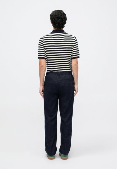 Polo a maniche corte a righe in navy e crema, abbinato a pantaloni scuri a righe sottili. Il tessuto sembra lavorato a maglia e texturizzato.