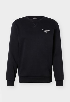 Melna džemperis ar apaļu kakla izgriezumu, gariem piedurknēm un baltu tekstu "BJÖRN BORG STOCKHOLM 1986" uz kreisā krūtīm augšējā daļā.