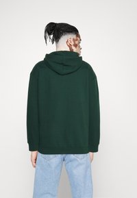 Groene hoodie met een relaxte pasvorm, lange mouwen en een grote capuchon. Gecombineerd met lichtblauwe denim jeans, wat een casual stijl toont.