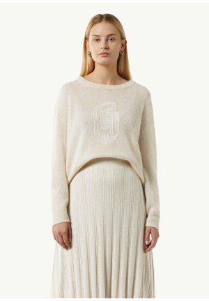 Light beige knit sweater with a crew neckline and subtle logo detail. Paired with a matching pleated midi skirt, both in soft textures.