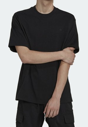 T-shirt en coton noir à col rond, manches courtes, avec un petit logo sur la poitrine, porté avec un pantalon cargo noir. Texture lisse.