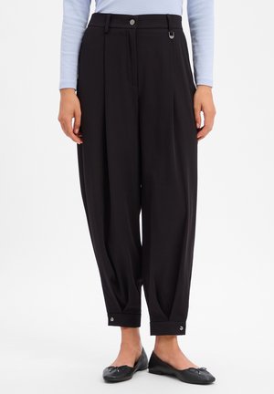 Zwarte, hoog getailleerde taps toelopende broek met knoopmanchetten, gecombineerd met zwarte ballerina's en een lichtblauwe top met lange mouwen.