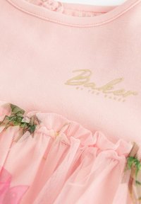 Rosa Kleid mit einem weichen Baumwolloberteil und einem gerafften Tüllrock, verziert mit Blumenmustern und einem goldenen Logo am Ausschnitt.