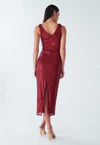 Sarkana kleita ar spīguļiem, V-veida aizmugure, pieguloša siluets, līdz ceļiem, ar sānu šķēlumu un šaurām siksnām. Gluda tekstūra ar spoguļojošiem akcentiem.