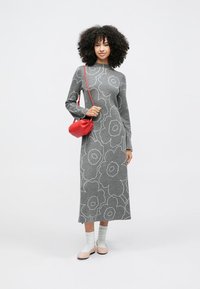 Šedé pletené šaty s květinovým vzorem, dlouhými rukávy, přiléhavým střihem a kulatým výstřihem. Nosit se bílé ponožky a červená kabelka přes rameno.