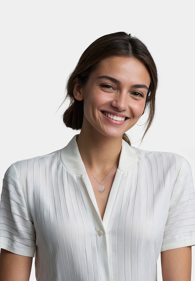 Hvid, kortærmet bluse med vertikale striber og krave. Et sølvfarvet hjerteformet halskæde er båret om halsen.