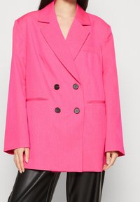 Rosa dubbelknäppt blazer i strukturerad tyg, stora slag, två framfickor och svarta knappar. Skräddarsydd, löst passform.