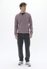 Helles lila, strukturiertes Sweatshirt mit V-Ausschnitt und Kragen, kombiniert mit dunkelgrauen Jeans und grauen Sportschuhen. Schlichtes, zeitgemäßes Design.