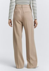 Beige wide-leg trousers made from smooth fabric, featuring two back pockets and a high waist. Striped long-sleeve top complements the look.