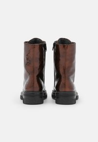 Bottes montantes en cuir verni marron à texture lisse, fermetures éclair latérales et semelles en caoutchouc noir robustes. Présente un design à bout arrondi.