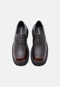 Mocassins en cuir marron à finition lisse, forme de bout rectangulaire, et semelle épaisse en caoutchouc noir. Dotés d'une bride décorative sur le cou-de-pied.