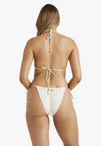 Vitt bikini med en texturerad yta, med justerbara knytband i ett mönster av grönt och krämfärgat samt små guldaccenter.