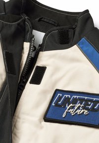 Zipjacka med en design i svart, kräm och blått. Inkluderar en texturerad lapp med "UNITED" och "future" i kontrasterande brodyr.
