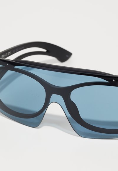 Ochelari de soare negri cu lentile mari, cu nuanță albastră, un design aerodinamic și un cadru din plastic neted. Prezintă o gravură subtilă a mărcii pe braț.
