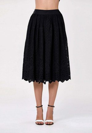 Jupe en dentelle noire longueur genou avec motifs floraux portée avec des talons hauts à bride cheville blancs et noirs sur les jambes du mannequin.