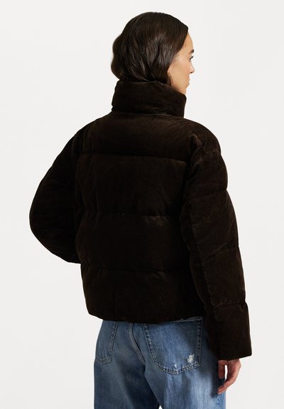 Brązowa kurtka puffer z korduroju z wysokim kołnierzem, pikowanym teksturą i szerokimi rękawami. Noszona z jasnoniebieskimi, przetartymi dżinsami.