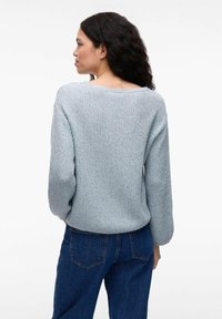 Jasnoniebieski sweter dzianinowy o luźnym kroju, szerokim dekolcie i długich rękawach, połączony z ciemnoniebieskimi dżinsami.