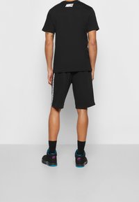 Černé tričko Nike s logem na zádech, spárované s černými šortkami s bočními pruhy a černými teniskami s modrými a růžovými akcenty.