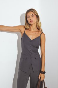 Gray sleeveless top with a V-neck, five buttons down the front, and two side pockets. Worn with dark pants and a brown handbag.