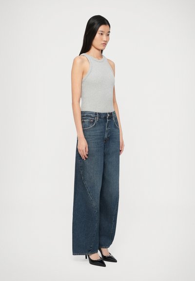 Ανοιχτό γκρι αμάνικη μπλούζα σε συνδυασμό με πλατύτερο σκέλος σκούρο μπλε τζιν και μαύρες ψηλοτάκουνες γόβες. Απλός σχεδιασμός με ομαλή υφή.