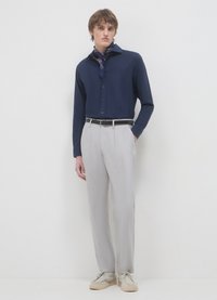 Marineblaue langärmlige Hemd, geknöpft, kombiniert mit hellgrauer strukturierter Hose und beigen Schuhen. Dazu ein blauer Schal mit Muster.