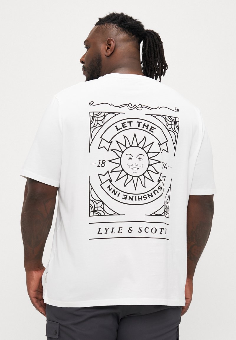 Valge lühikeste varrukatega t-särk, millel on julge must päikesegraafika koos tekstiga "LASKE PÄIKESEL SISE RONIDA" ja "LYLE & SCOTT" luksuslikus raamis.