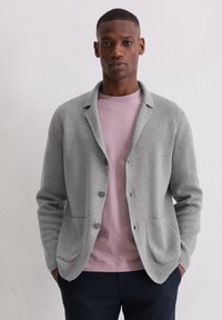 Hellgrauer Cardigan mit einem Schalkragen, zwei vorderen Taschen und drei Knöpfen, getragen über einem rosa Rundhalsausschnitt-T-Shirt. Einfarbig, weiche Textur.