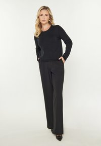 Pulover negru tricotat cu mâneci lungi și decolteu rotund, accesorizat cu pantaloni negri cu talie înaltă și picioare largi, împreună cu pantofi negri cu vârful ascuțit.