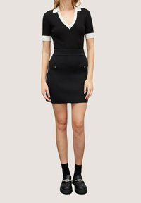 Czarna sukienka z prążkowanej tkaniny, z białym kołnierzykiem, krótkimi rękawami i dwiema przednimi kieszeniami. Połączona z czarnymi butami i skarpetkami do kostek.
