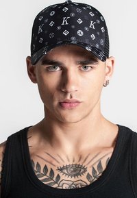 Gorra negra con un patrón repetitivo de letras y símbolos. Presenta un Visera curvada y una parte trasera ajustable de malla texturizada.