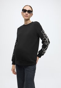 Μαύρο φούτερ με μακριά μανίκια και λευκή κεντητή λουλουδάτη διακόσμηση στο αριστερό μανίκι. Απαλό ύφασμα, άνετη εφαρμογή, σχέδιο με στρογγυλή λαιμόκοψη.