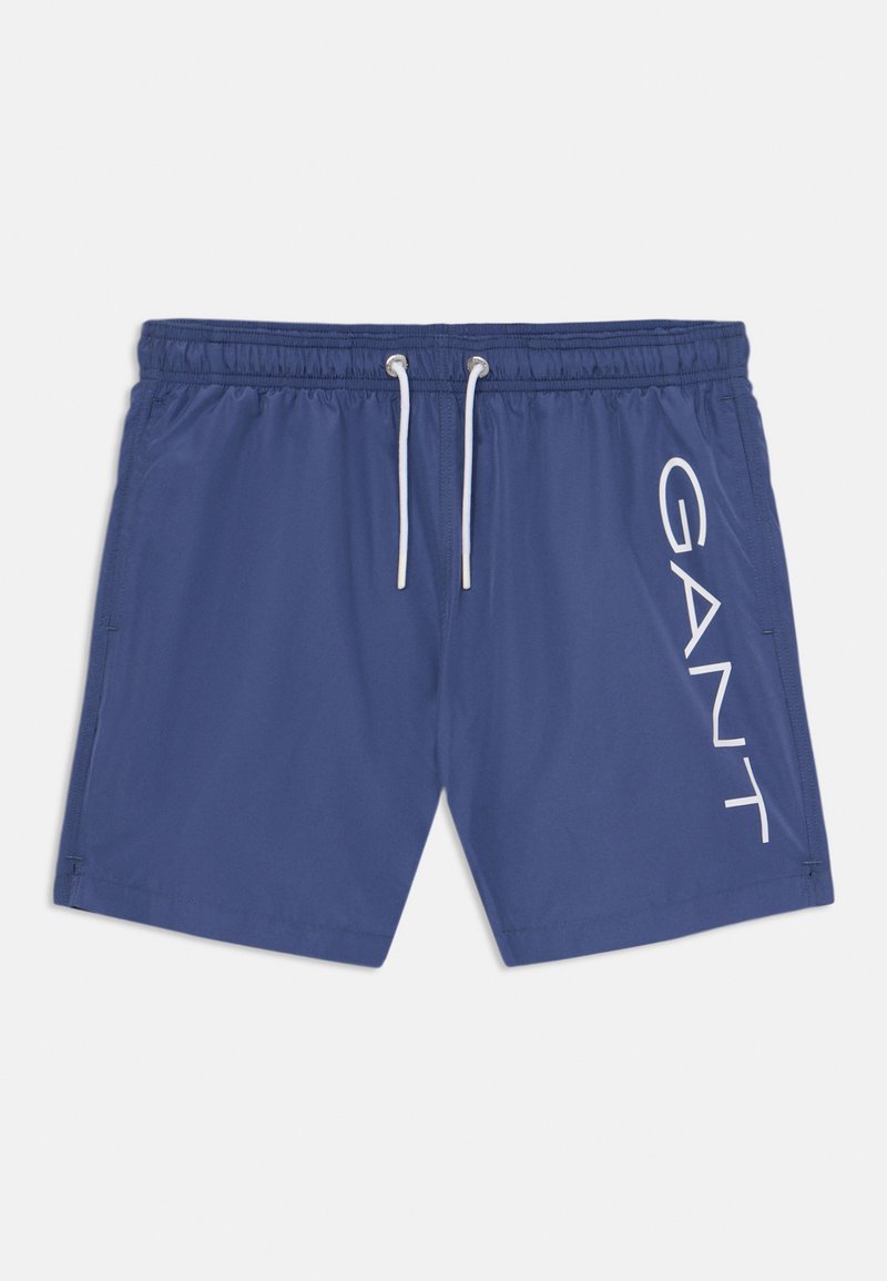 Pantaloni da mare blu navy con vita elastica, cordino bianco e grande logo "GANT" stampato verticalmente sul lato sinistro. Tessuto liscio.