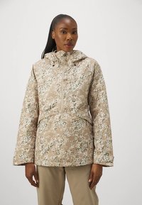 Beige waterproof jacket featuring a floral camouflage pattern, a hood, and a zip closure, with wide sleeves and a relaxed fit.