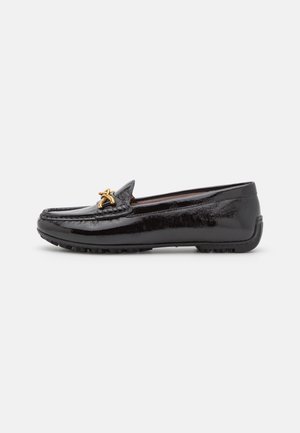 Mocassin en cuir noir brillant avec boucle décorative dorée et semelle en caoutchouc, profil latéral sur fond clair uni.