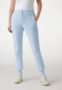 Light blue joggers made of soft fabric, featuring a drawstring waistband, tapered legs, and ribbed cuffs; side pockets and logo detail present.