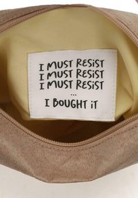 Pouch in suede marrone con un interno in tessuto giallo, con un'etichetta etichettata con testo nero che ripete "DEVO RESISTERE" e termina con "L'HO COMPRATO."