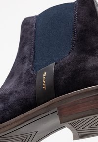 Marineblauwe suède enkelboot met elastische zijpaneel, voorzien van een zwart leren label met gouden "GANT" logo en een gestructureerde rubberen zool.