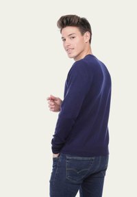 Pull en maille bleu marine avec des manches longues, un col rond et des poignets côtelés, porté sur un jean bleu foncé, présentant un design ajusté et une texture lisse.