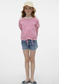 Top a maniche lunghe a righe rosa e bianche con nodo frontale, abbinato a pantaloni corti in denim. La modella indossa un cappello di paglia e scarpe slip-on.