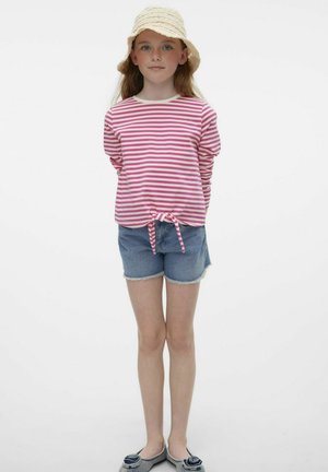 Roze en witte gestreepte langharige top met een knoop aan de voorkant, gecombineerd met denimshorts. Het model draagt een geweven zonnenhoed en instapschoenen.