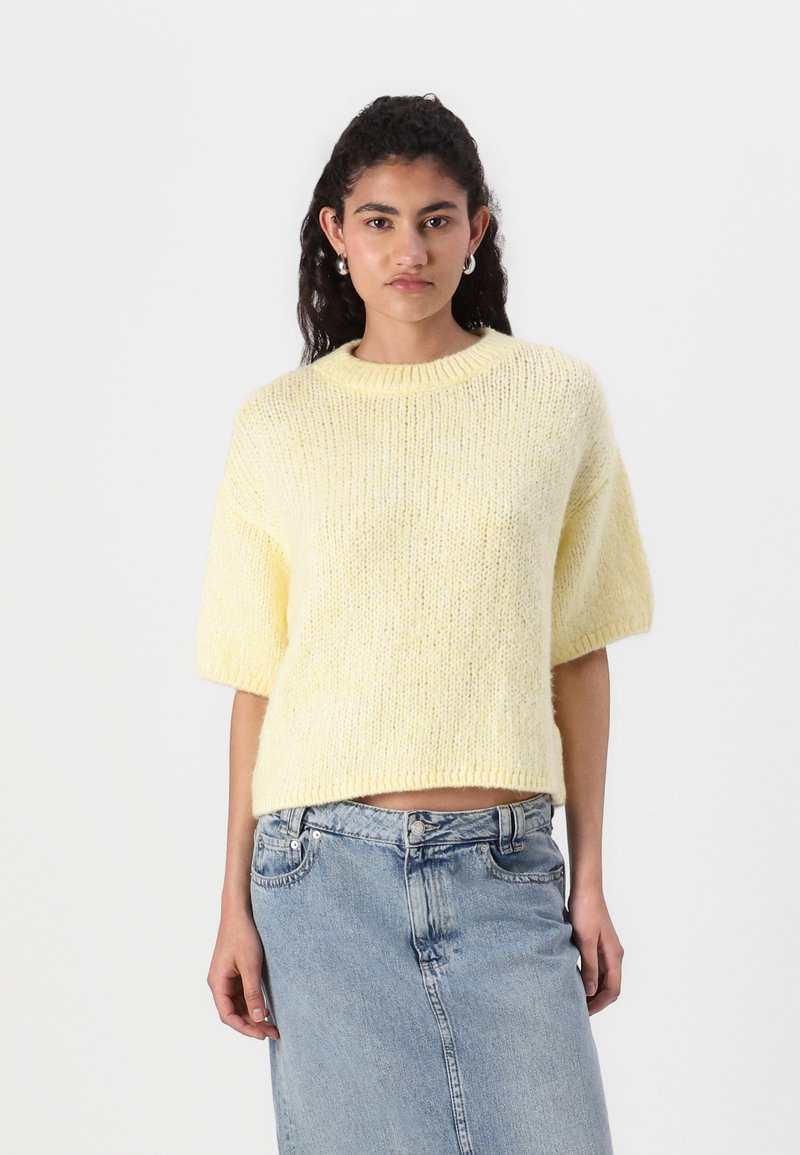 Kortermet gul strikkegenser med rund hals, med en myk tekstur og løs passform, kombinert med et blått denimskjørt.
